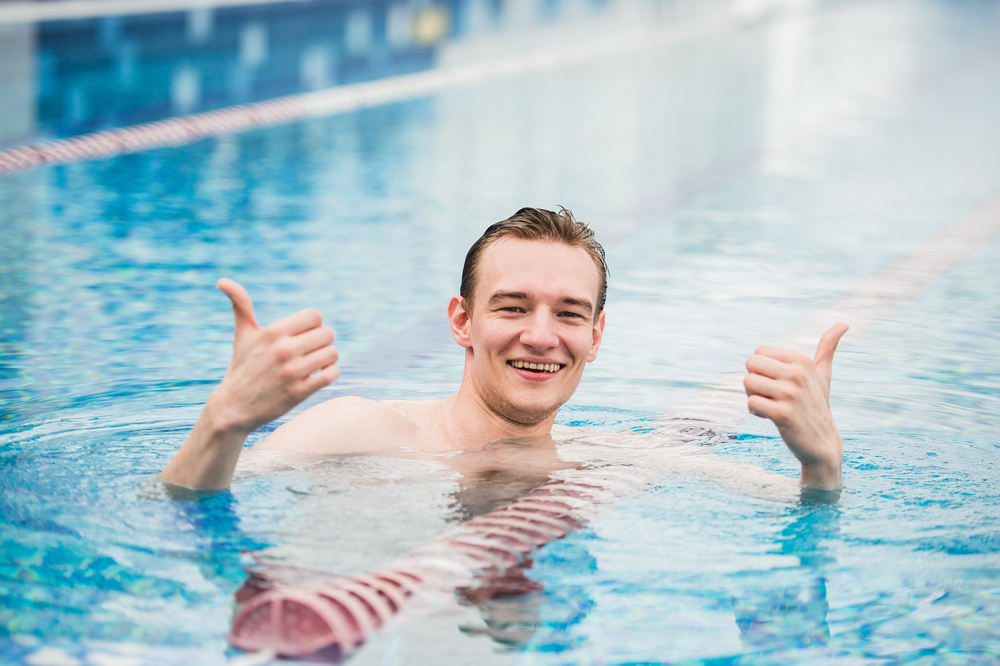 Person in a swimming pool, looking towards the camera and smiling while holding two thumbs up