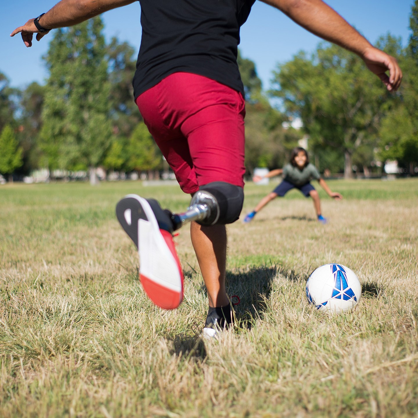 Man with prosthetic leg kicking football to child