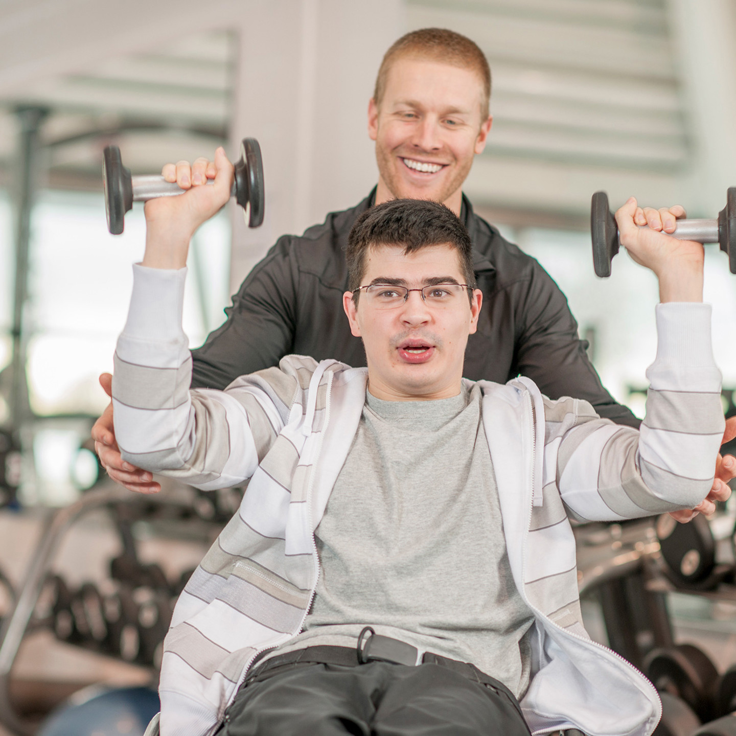 Man lifting up dumbbells at the gym with assistance